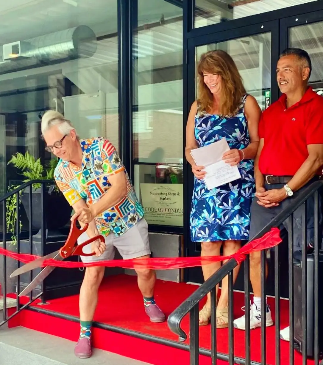 A colorful ceremony showing three individuals, with one cutting a ribbon and others holding papers, celebrating a special event.