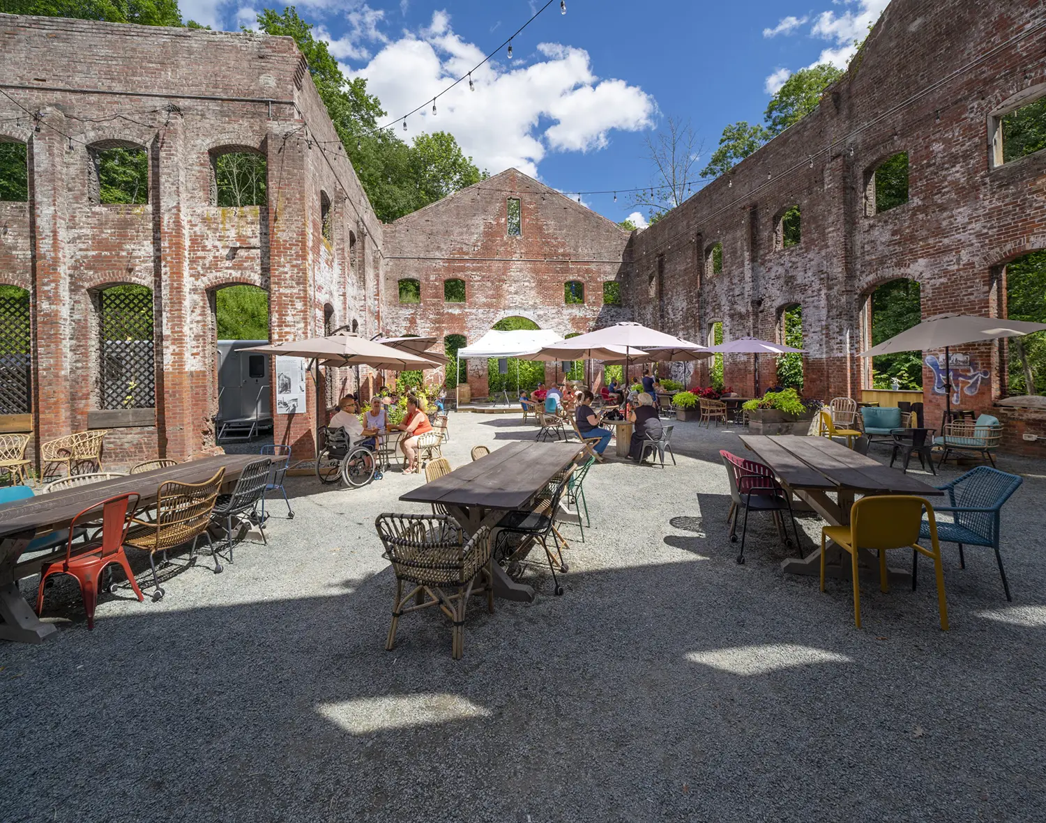An outdoor café with various seating arrangements in a historic, partially ruined building, surrounded by greenery and open skies.