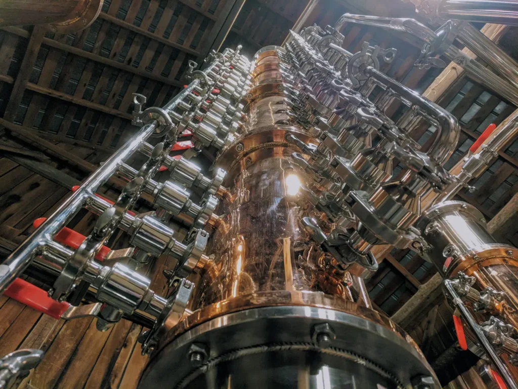 A close-up view of a complex distillation apparatus, showcasing intricate pipes and valves, reflecting a blend of metal finishes and industrial design.