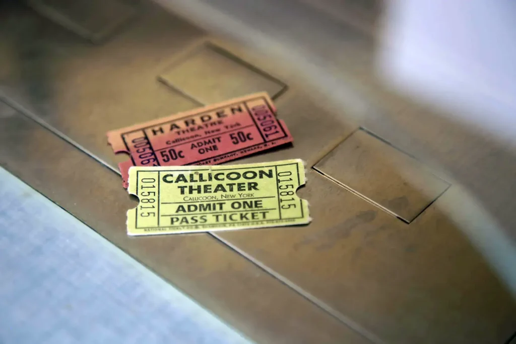 Two vintage theater tickets, one red labeled 'Harden' and one yellow for 'Callicoon Theater', resting on a metallic surface.