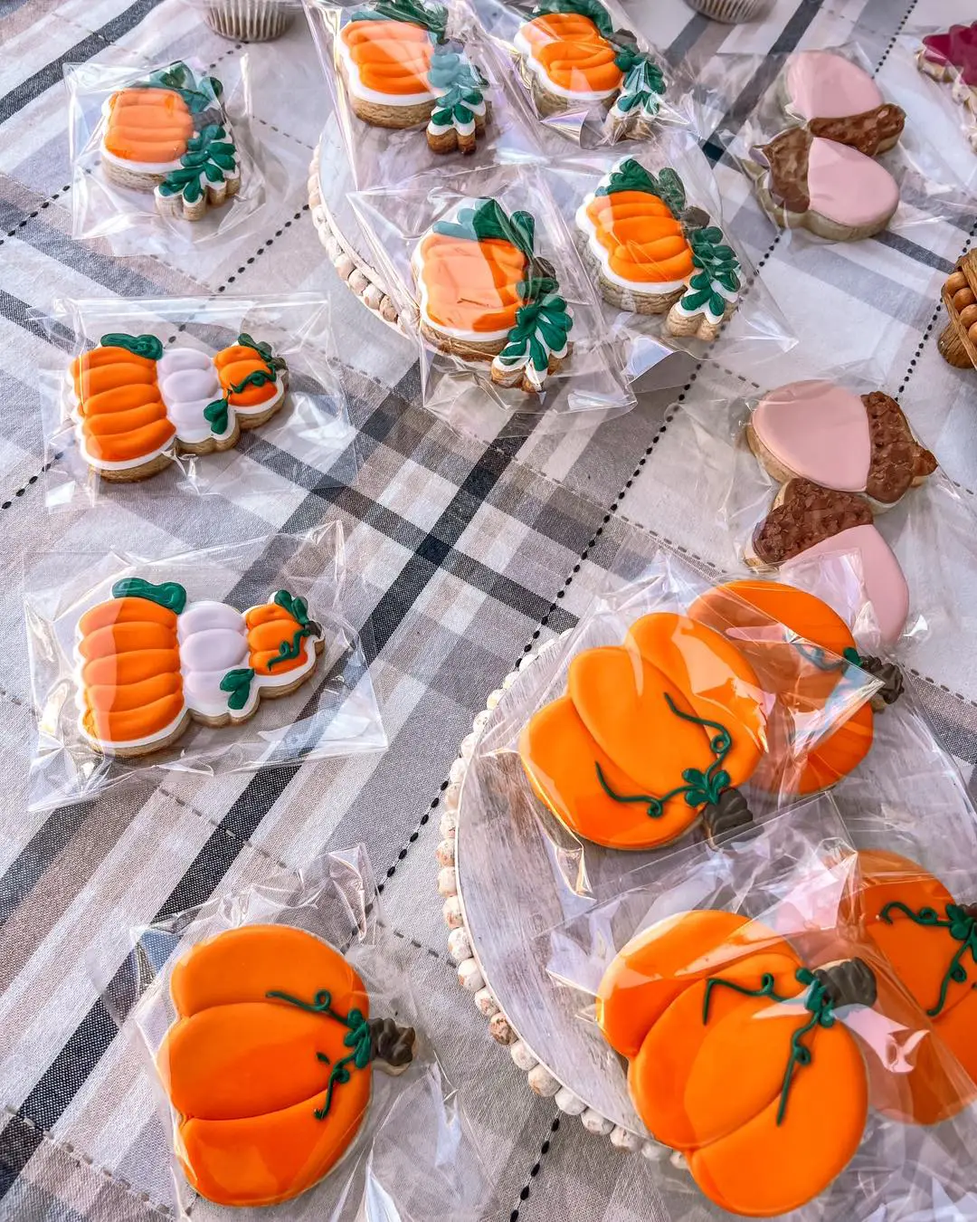 Colorful autumn-themed cookies shaped like pumpkins, decorated with green icing, arranged on a tablecloth.