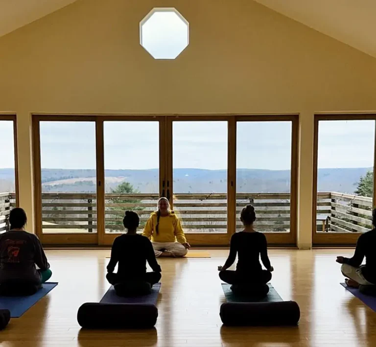 A serene yoga class in a spacious room with large windows overlooking mountains, focusing on meditation and mindfulness.