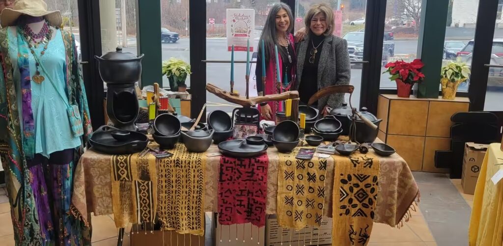 Two women at a business expo showcasing handcrafted pottery, textiles, and artisanal products.