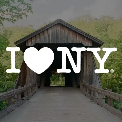 A wooden bridge under a cloudy sky, with the iconic 'I ❤️ NY' logo prominently displayed.