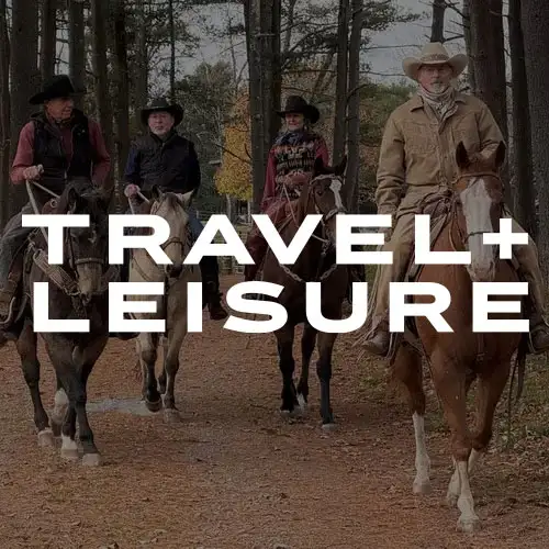 A group of four horseback riders clad in western attire, traversing a wooded path in autumn.