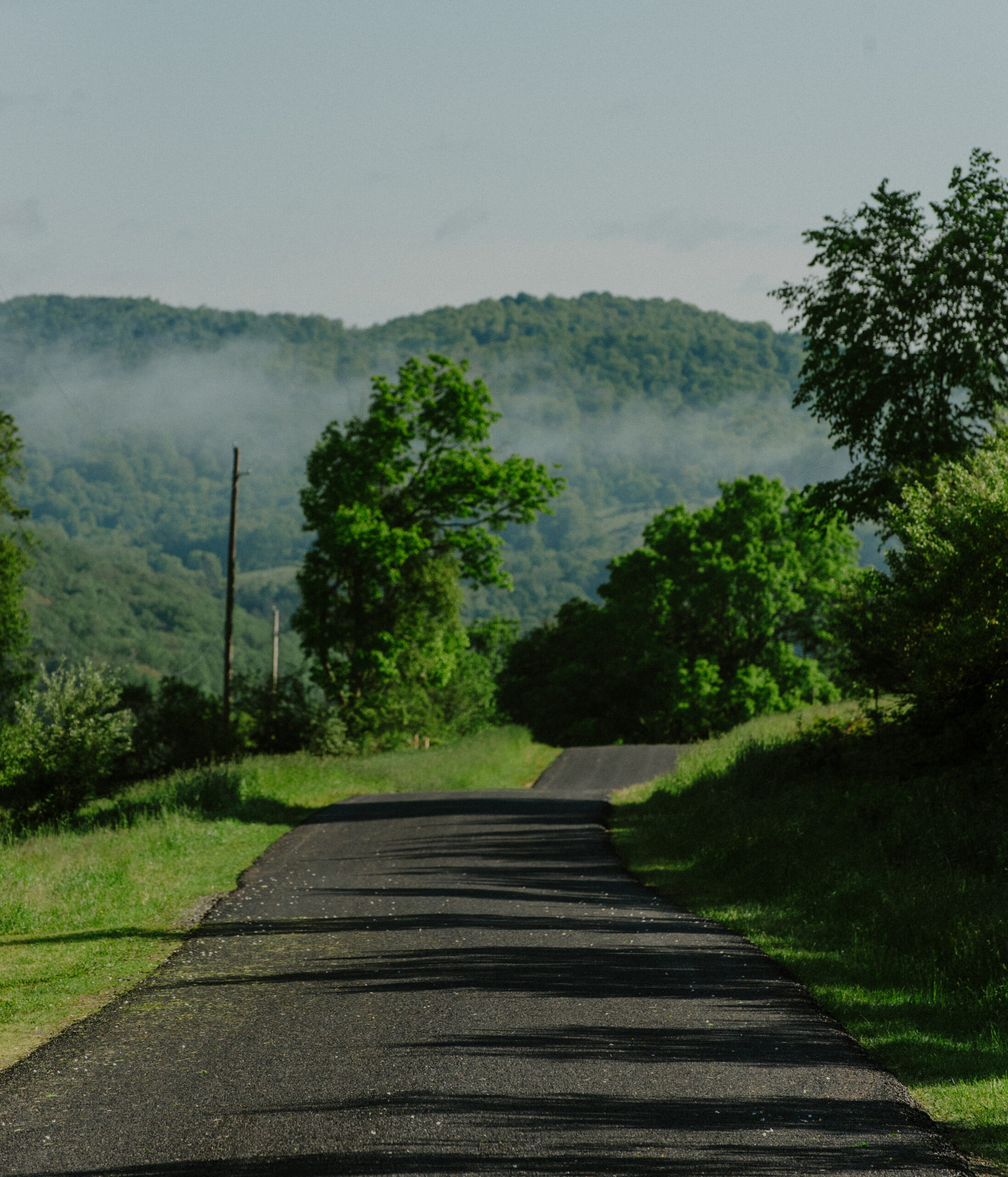 A scenic country road through the Catskills in Sullivan County with green landscape and mist in the background.
