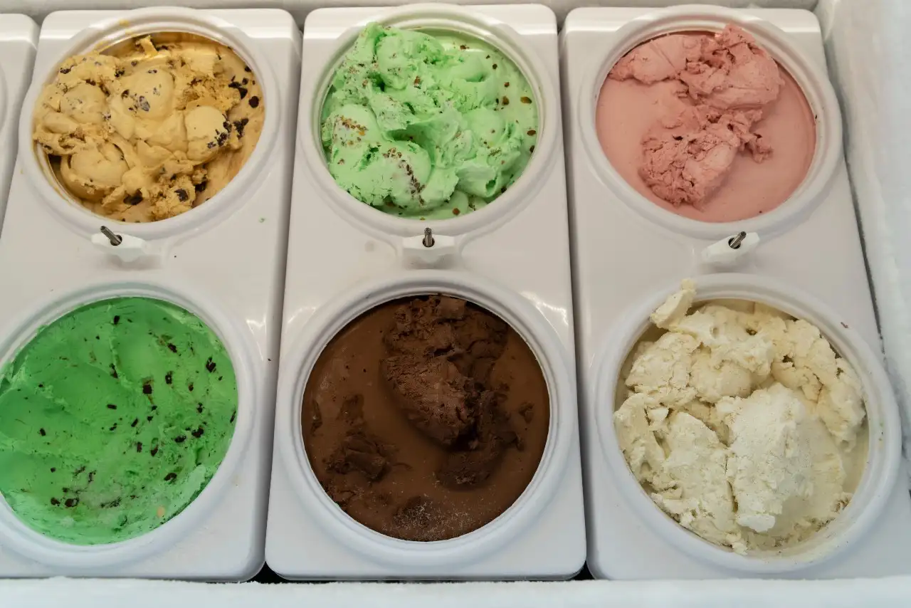 An array of ice cream flavors in containers, including mint, chocolate, strawberry, and more, presented in a freezer display.