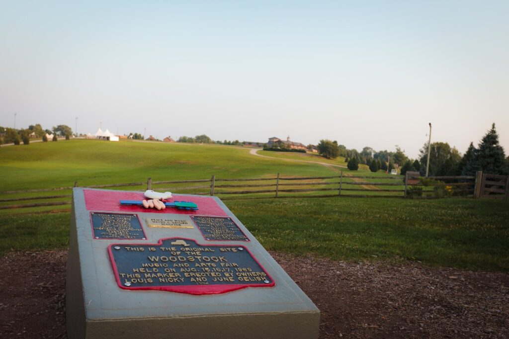 A memorial stone and plaque dedicated to Woodstock with the famous field in the background.