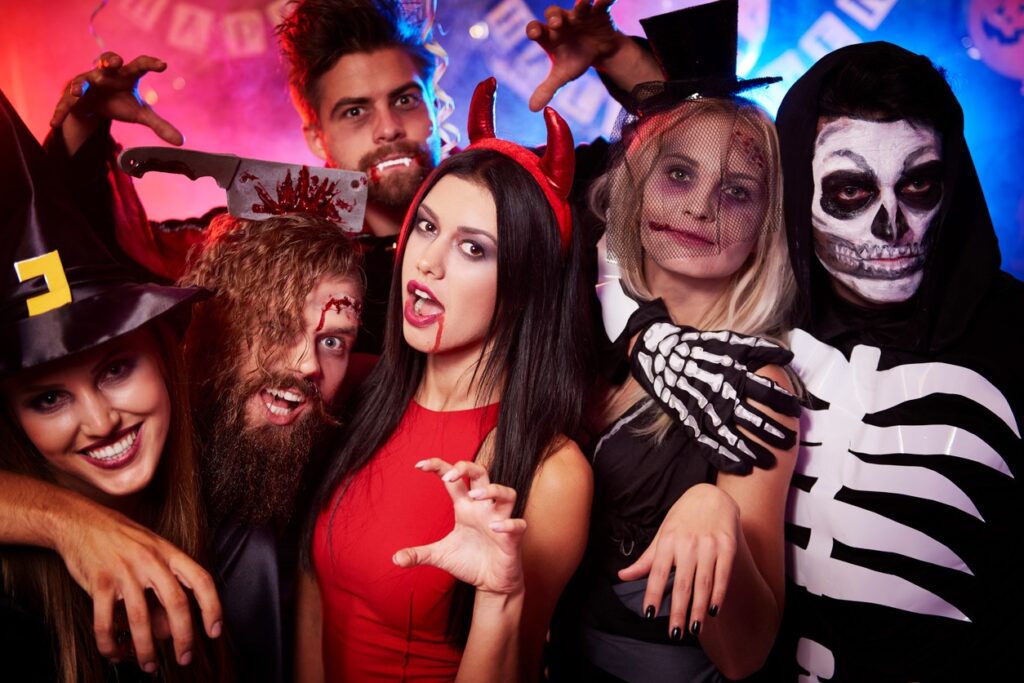 A group of adults makes scary faces dressed in Halloween costumes. 