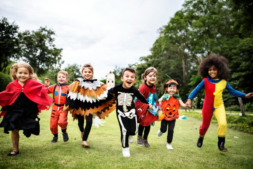 Kids in Halloween costumes run at the camera through a park. 