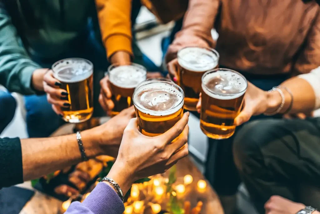 A group of people cheerfully raising glasses of beer in a social gathering, with a warm and cozy atmosphere.