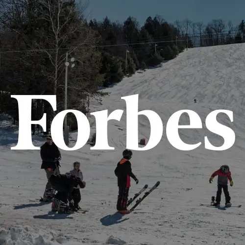 Skiers and children enjoying a snow-covered slope, with trees and ski infrastructure in the background.
