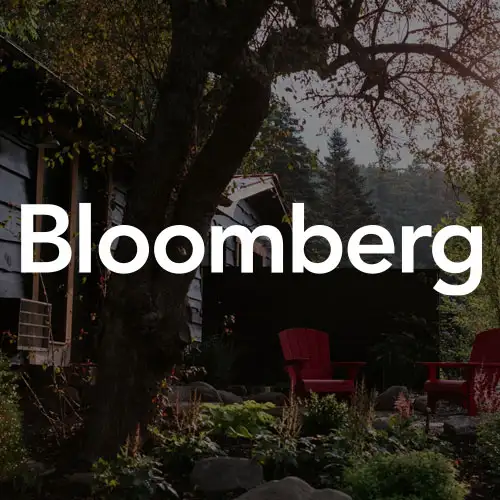 A serene garden scene featuring a black structure, a tree, and red chairs, illuminated by warm sunlight.