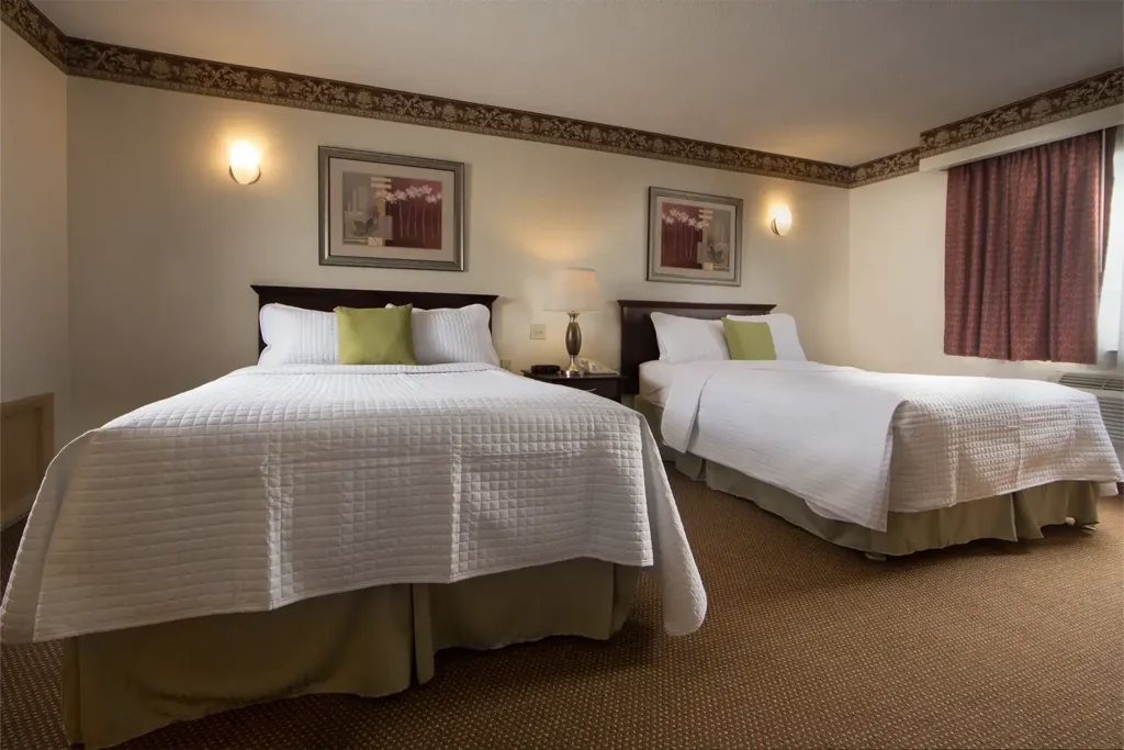 A cozy hotel room with two neatly made beds, soft lighting, and decorative wall art, creating a warm and inviting atmosphere.