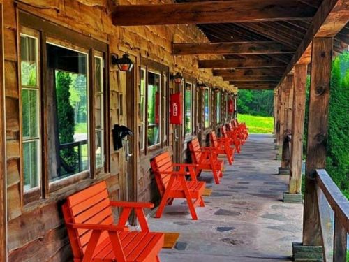 A charming wooden porch with bright orange chairs, featuring multiple windows and a serene green landscape in the background.