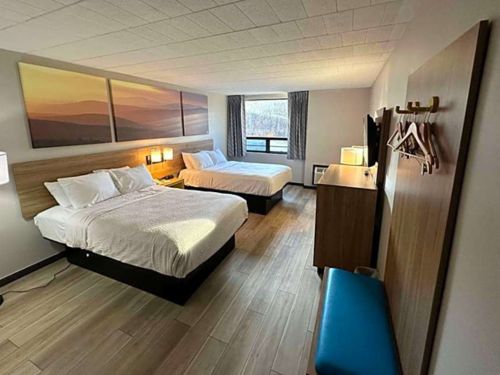 A modern hotel room with two beds, wooden furnishings, a large window, and artwork on the walls, showcasing a clean and welcoming atmosphere.