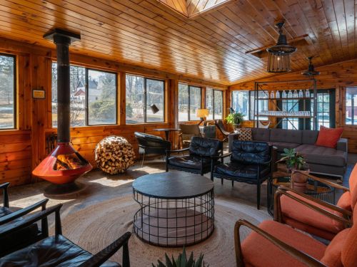 A cozy sunroom featuring wooden walls, various seating options, a circular coffee table, and large windows allowing natural light.
