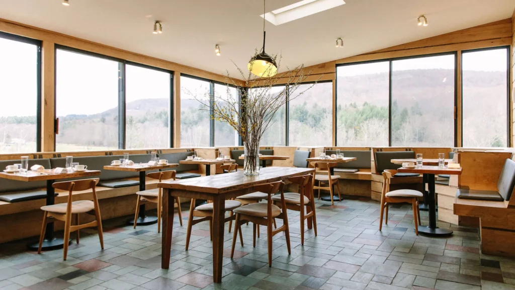 A bright, modern restaurant interior featuring wooden furniture, large windows, and scenic views of the outdoors.