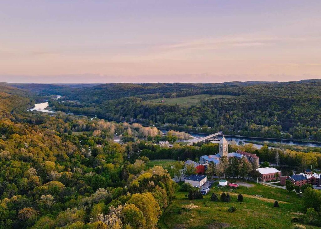 A scenic landscape showing a river winding through lush green hills and an old building surrounded by trees.