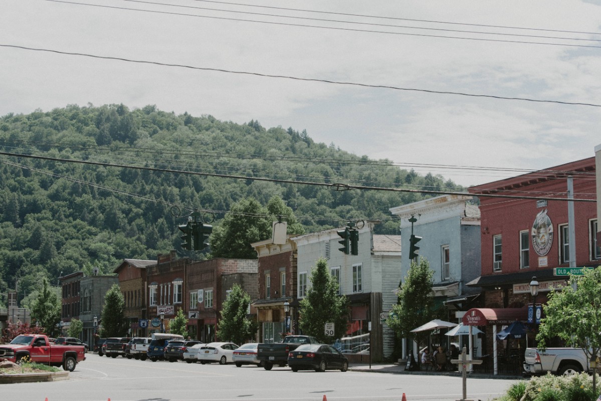 Main street in Roscoe with various shops, surrounded by green hills and trees under a partly cloudy sky.