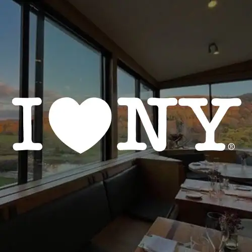 A cozy restaurant interior featuring a large window with scenic views, highlighted by the iconic 'I ♥ NY' logo.