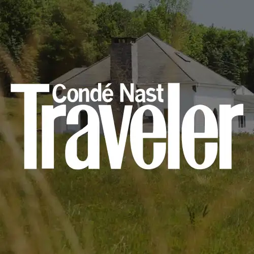 A peaceful rural scene with a modern white house nestled among green trees and grasses, set against a clear sky.