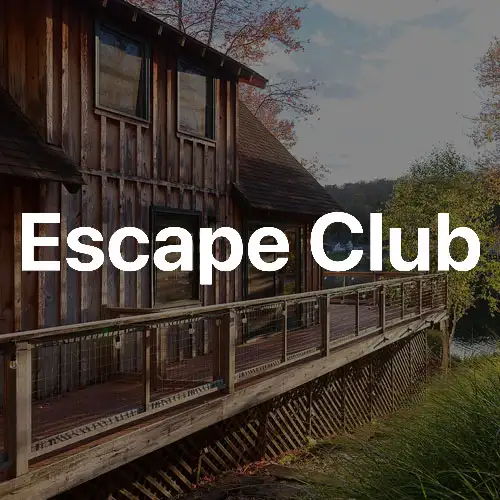 A rustic wooden building beside a serene body of water, surrounded by lush greenery and trees in a tranquil setting.