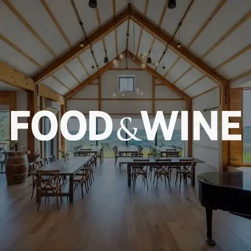 A spacious dining area with wooden furniture, large windows, and a grand piano, emphasizing a warm and inviting atmosphere for food and wine experiences.