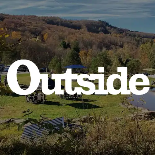 A scenic outdoor area with green fields, autumn foliage, and a peaceful pond under a clear sky.