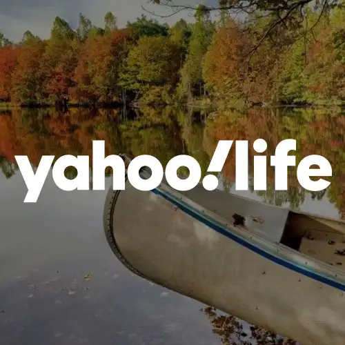 A serene lake reflects vibrant autumn foliage, with a canoe resting at the shore.