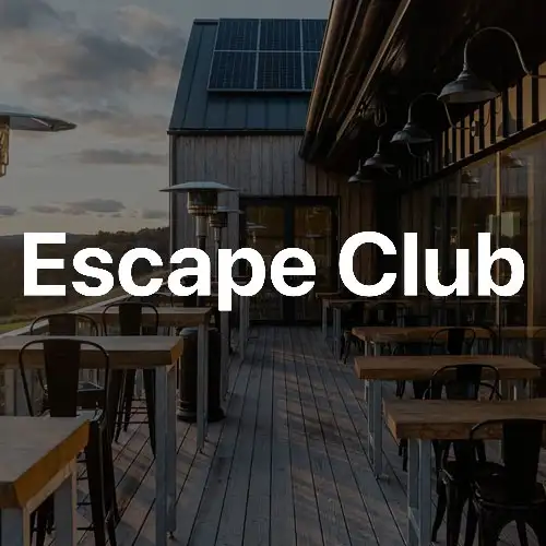 An outdoor terrace with wooden flooring, tables, and chairs, featuring modern architecture and a backdrop of clouds and a solar panel.