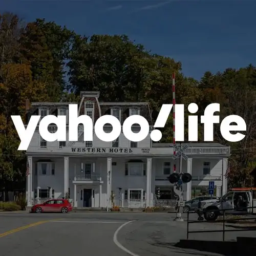 A historic hotel building with a white facade and colorful trees in the background, overlaid with the text 'yahoo!life'.