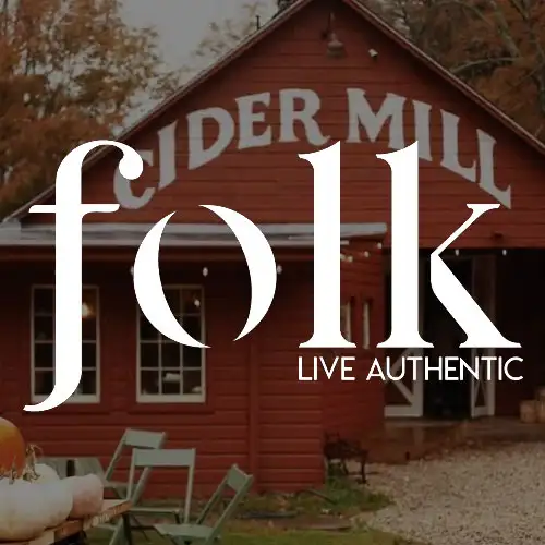 A rustic red barn displaying the words 'CIDER MILL' with seating and autumn decor in the foreground.