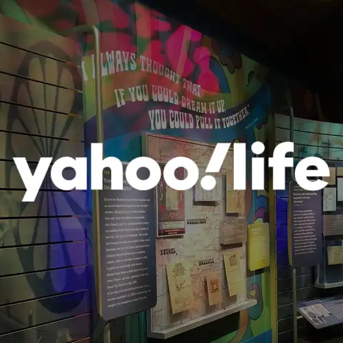 A colorful exhibit wall with various posters, text, and the logo of Yahoo Life prominently displayed.