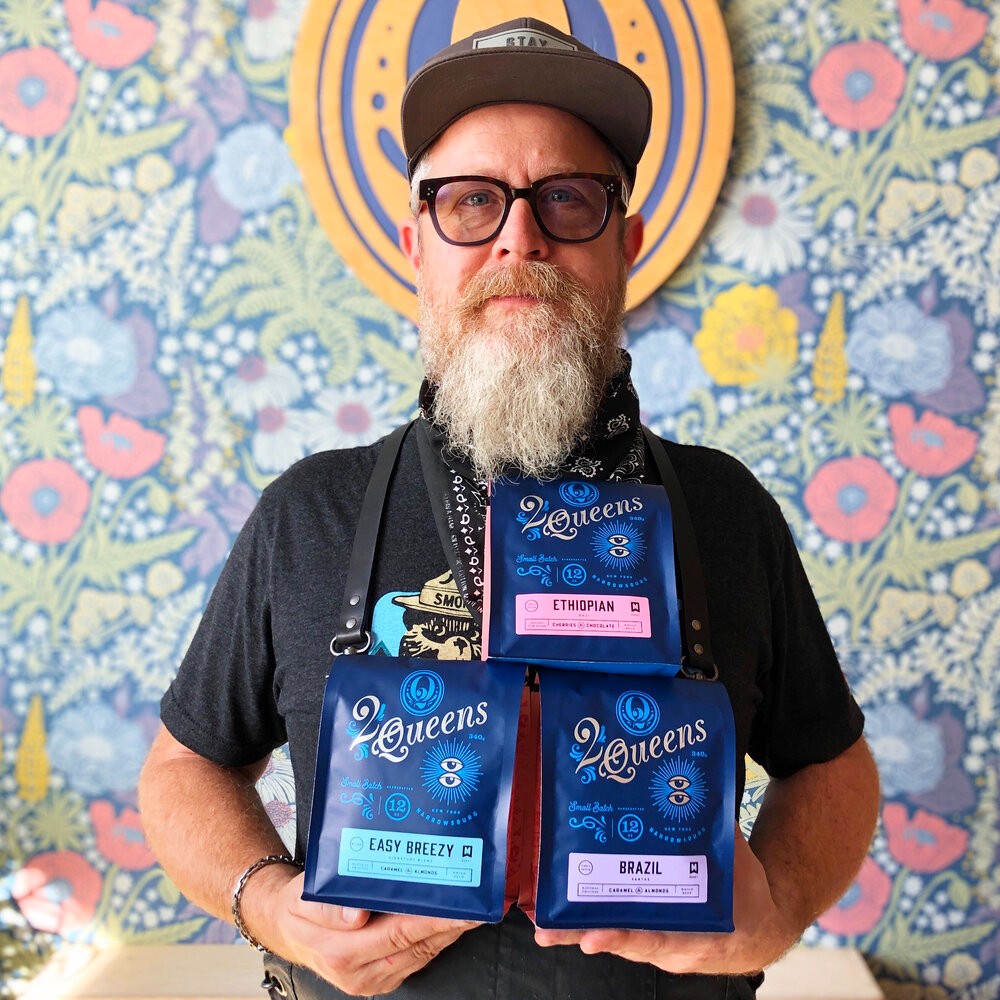 Martin, co-owner of 2 Queens Coffee, holds bags of their roasted coffee.