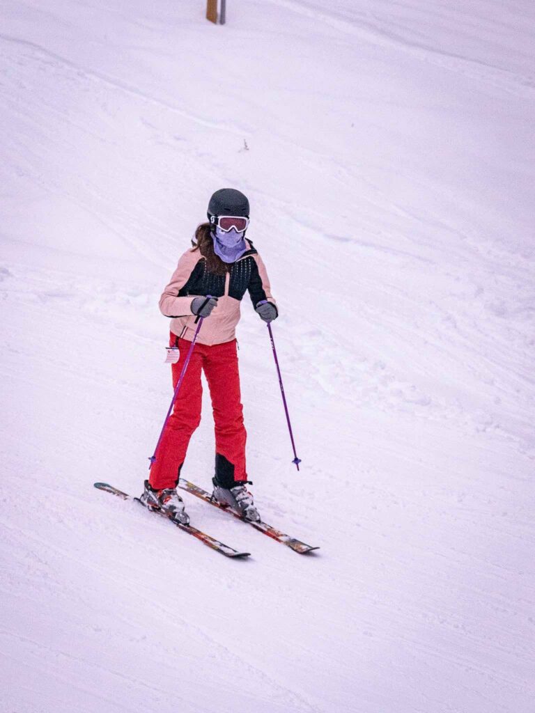 A skier glides down a snow-covered slope, wearing a helmet, goggles, and bright red pants amidst a winter landscape.