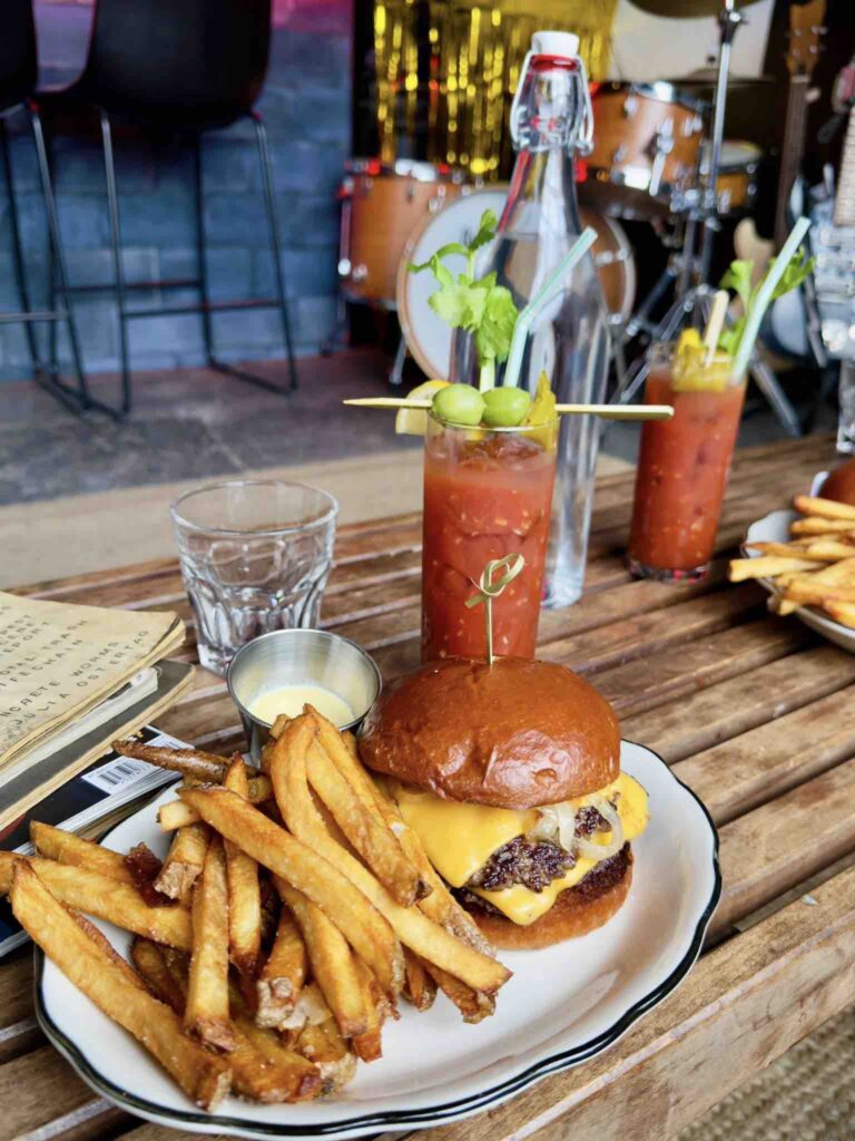 A delicious cheeseburger with golden fries and a colorful cocktail, set on a rustic wooden table in a vibrant atmosphere.