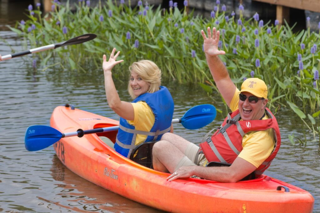 Two kayakers waving and smiling while on the river.