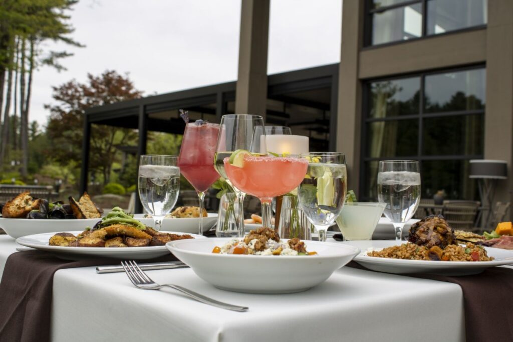 A gourmet meal and cocktails are set at a table with a white tablecloth on the outdoor patio of The Eldred Preserve in the Sullivan Catskills.